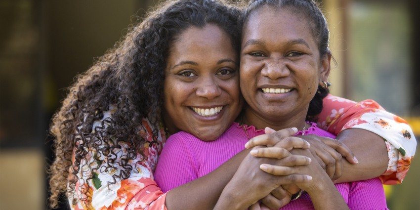 Two young aboriginal female students outdoors with their arms around each other smiling at the camera