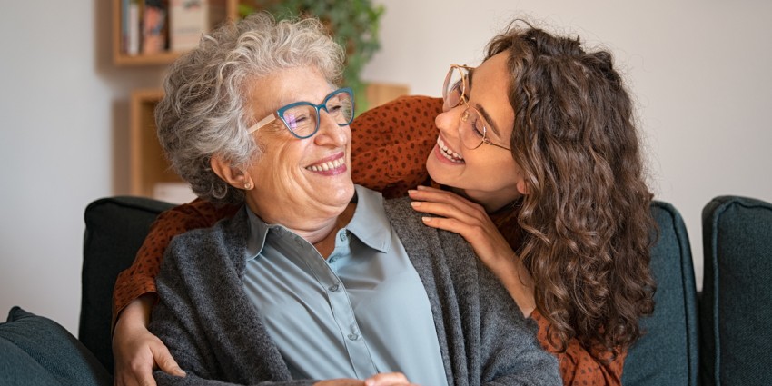 Elderly woman and young adult woman hugging at home and looking at each other