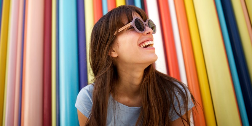 Close up of cheerful young woman laughing with sunglasses against a colourful background