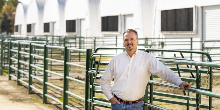 Publicity shot of Prof. Frank Mitloehner on farm property. Fences and barns in background.