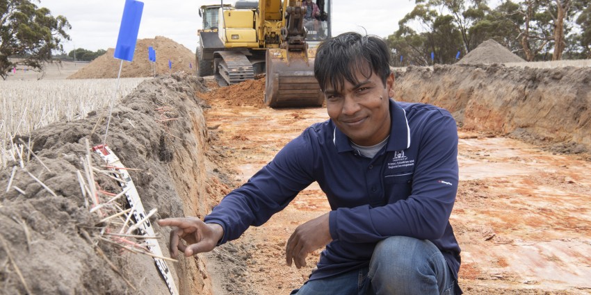Dr Gaus Azam in a trial plot at Meckering, excavator and scraper vehicles in background.