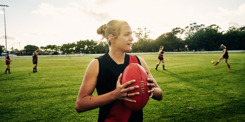 A group of young women doing Aussie Rules Football training on a grassed oval