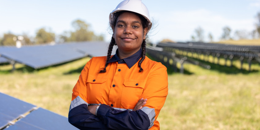 A young resilient-looking Aboriginal woman in mining work clothes in an outdoor environment with her arms folded