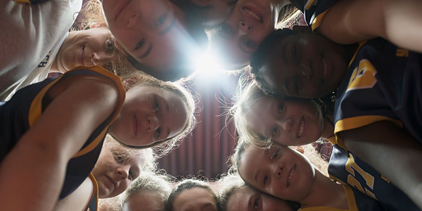 A group of young people in a huddle looking down at the camera.