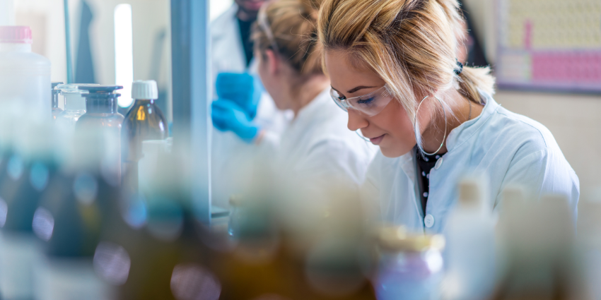 Image of a young female scientist working at a laboratory, with two other scientistsin the background/