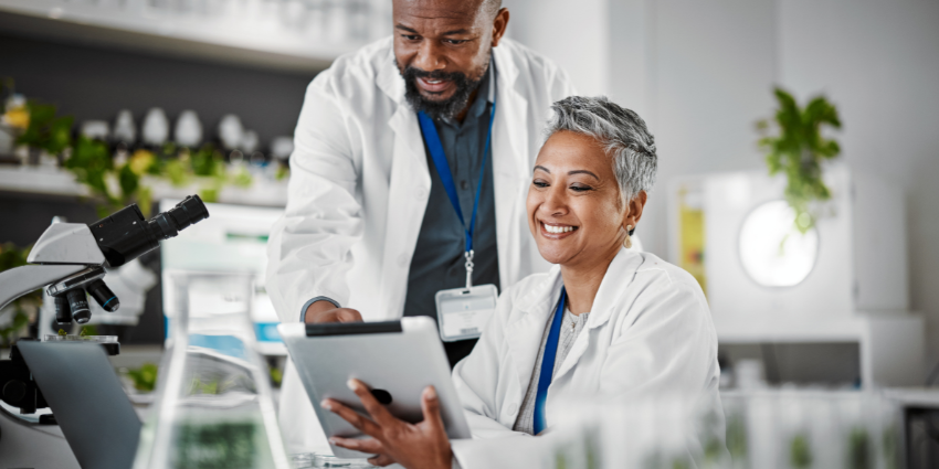 Image of two researchers in a medical laboratory, dressed in white lab coats and looking at a tablet 