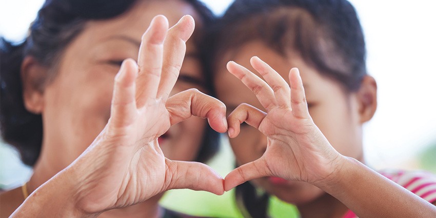 Image of a woman and a child with their hands forming a love heart shape