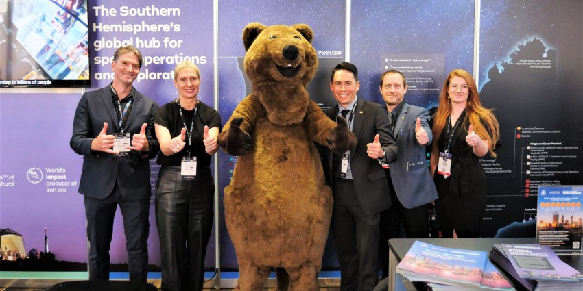 A group photo in front of the Department of Jobs, Tourism, Science and Innovations booth. From left to right is Ash Boddy, Linda Dawson, A person in a Quokka suite, James Yuen, Simon Aaron and Kirilly O'Reilly. Everyone has their thumbs up.