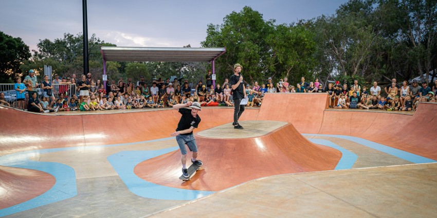 Photo of someone skating in a skate competition in front a big crowd of young people 