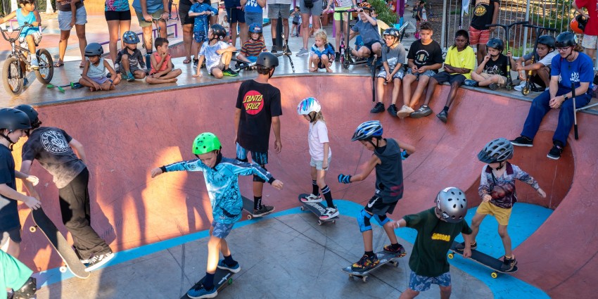 photo of a group of young skateboarders with young people and parents watching on