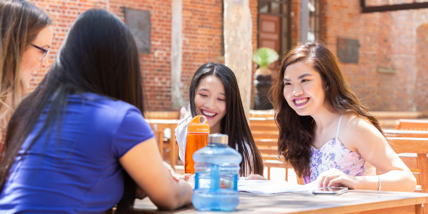 group of girls sitting at picnic table in sun and smiling