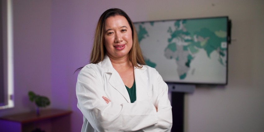 A woman in a lab coat stands confidently in front of a television, showcasing her professional demeanor in a laboratory setting.