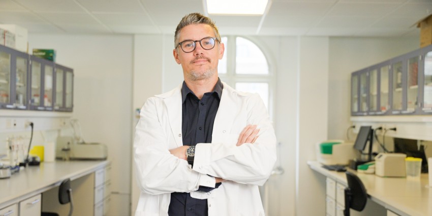 A man in a lab coat stands confidently in front of a desk, showcasing a professional laboratory environment.