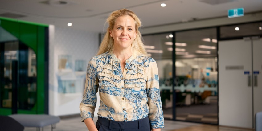 A glowing Pamela Laird looks to the camera with a gentle smile. Oe hand placed in her pant pocket.