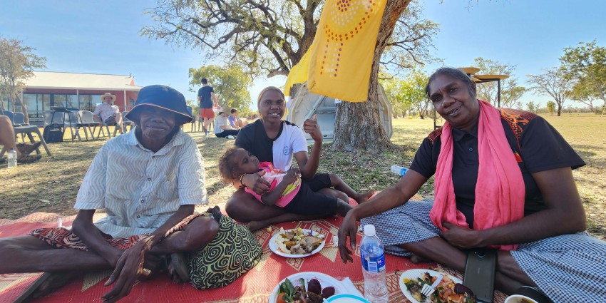 A group of 4 individuals sitting on a picnic blanket with plates of food in front of them.