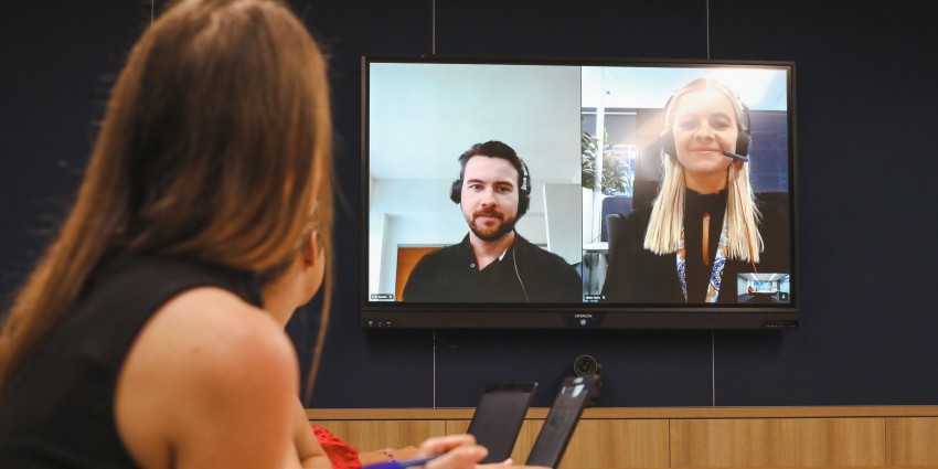A photo of people in a meeting with two people joining online whom are visible on a large screen