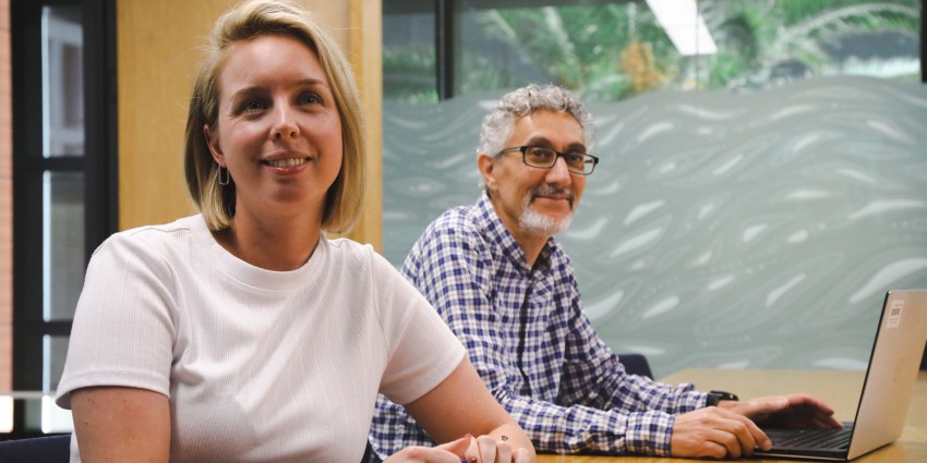 A picture of two people sitting at a desk smiling at the camera