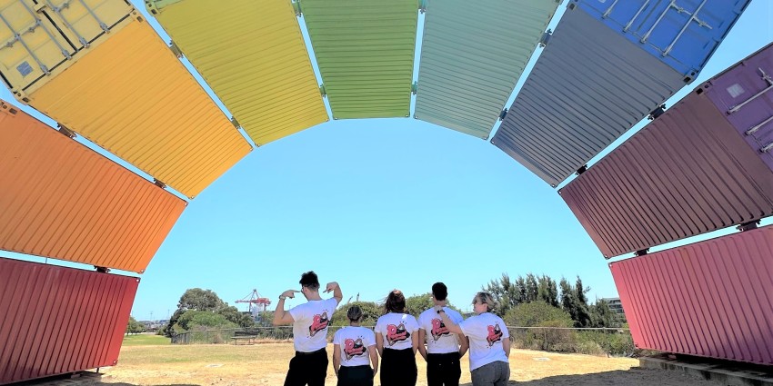 A picture of 5 people standing under a rainbow made of shipping containers
