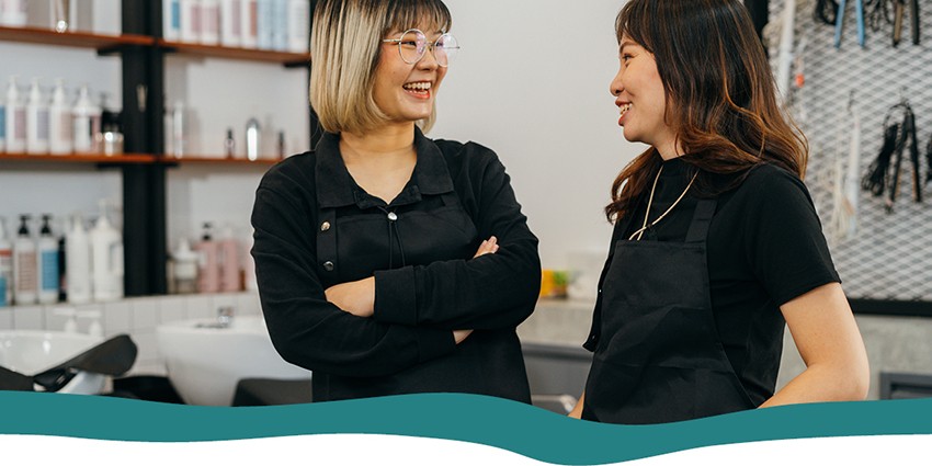 Two female hairdressers smiling at one another in the hair salon