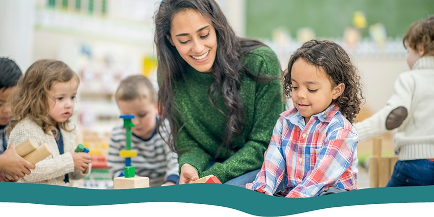 A teacher playing with building blocks with a child in the classroom