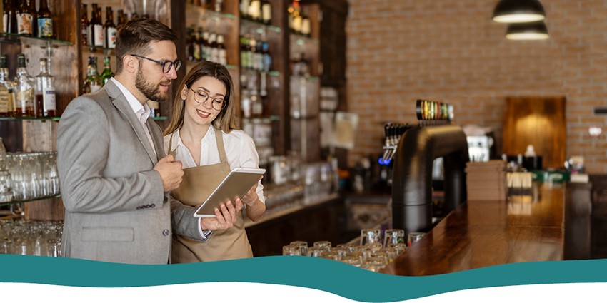 A restaurant worker and a businessman both looking at a tablet behind the bar