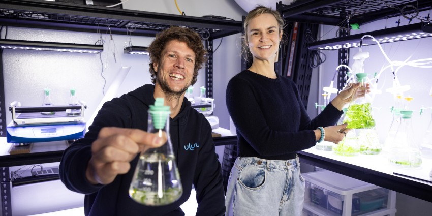 two young scientists, one male, one female in lab holding test tubes and vials with green liquid