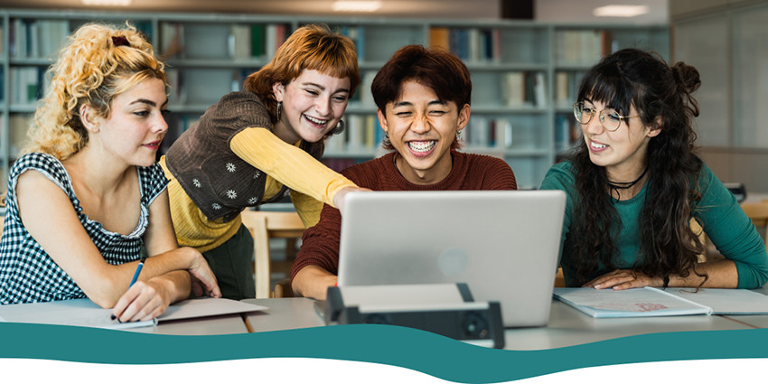 teenagers gathered around a laptop in a library