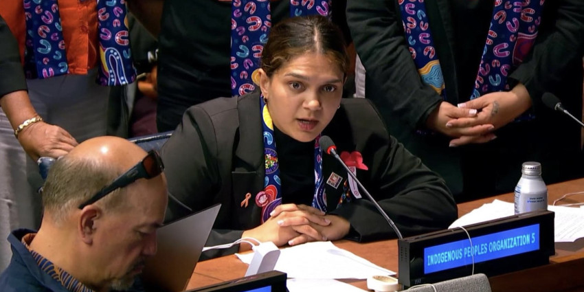 A young Aboriginal woman speaking into a microphone, with an audience watching on
