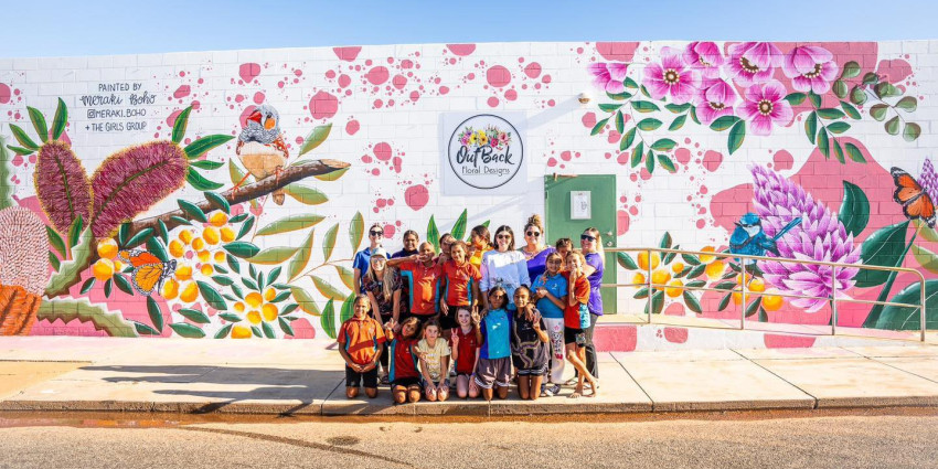 group photo of a group of Aboriginal girls and women on a street with a colourful mural on a wall behind them