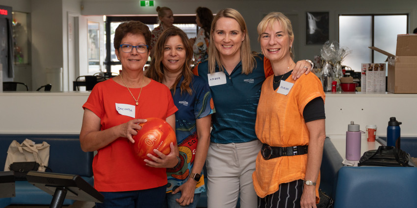 Photo of a group of four women wearing colourful clothing and smiling, in a casual indoor setting
