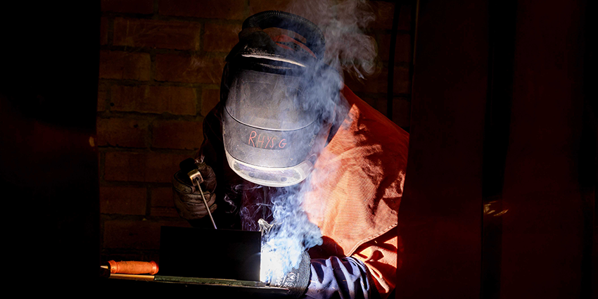 Individual welding steel with visible smoke and protective gear.