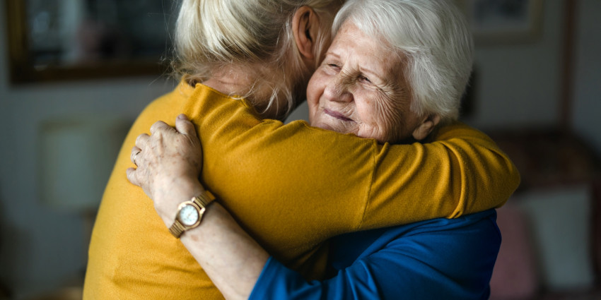 Two woman pictured in a hugging embrace, as if to comfort each other