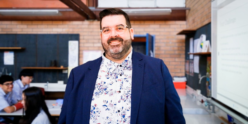 Nathan standing in his classroom with some students in the background 
