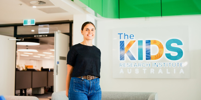 Taleah standing in front of The Kids Institute sign 