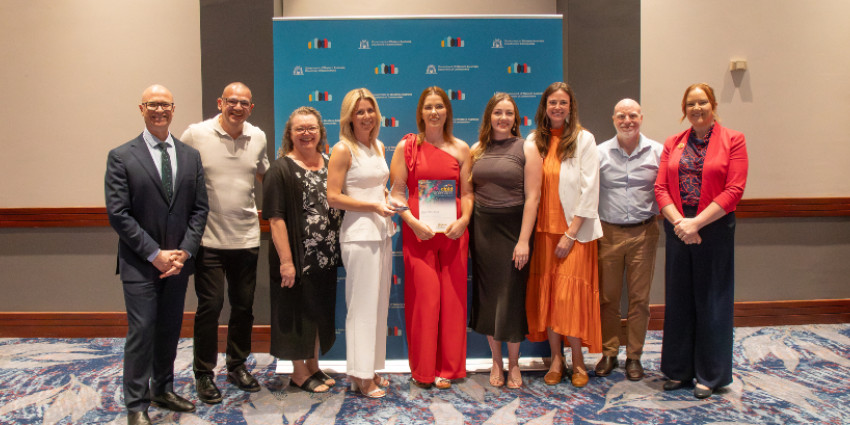 group photo of 9 adult people on stage at an event