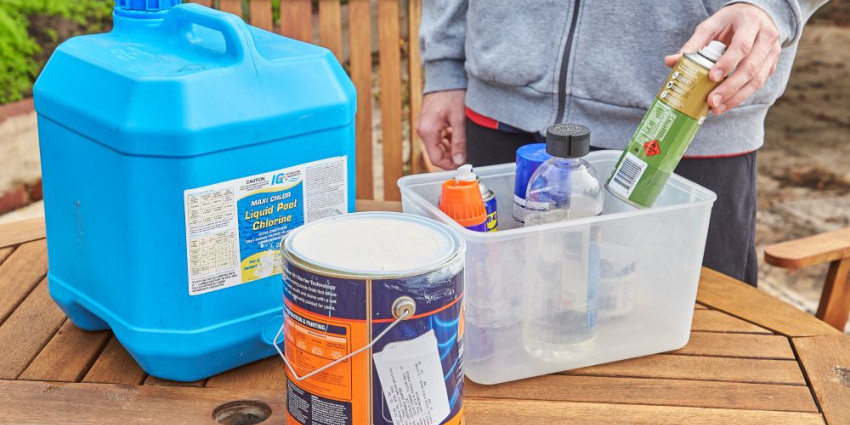 A collection of Household Hazardous Waste on an outdoor table, including a paint tin, chlorine container and aerosol cans.