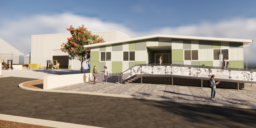 A modern green‑and‑white building with an accessibility ramp in front, with people walking nearby and industrial sheds and forklifts in the background on a sunny day.