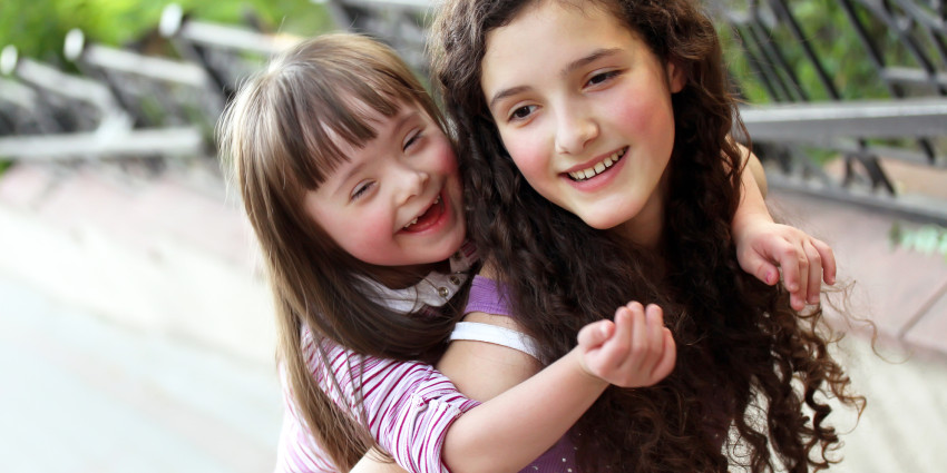 A young teenage girl smiling, carrying a young happy child on her back