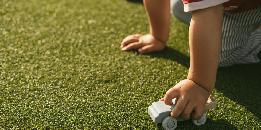 a child's hand holding a toy car on the grass