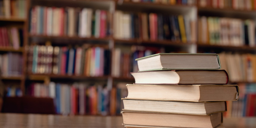 several books stacked on a table with a bookshelf in the background full of books