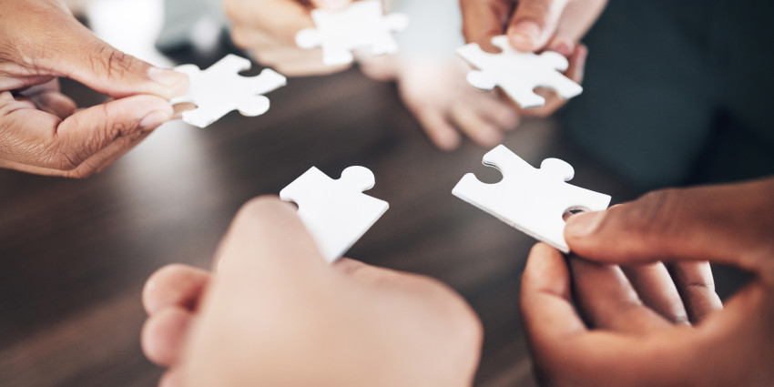 Five hands reaching forward, each and holding a piece of a jigsaw puzzle