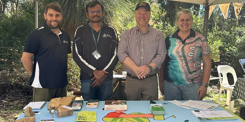 Four people standing behind a Treebate information stall under a gazebo at an outdoor community event, with brochures and displays on the table.