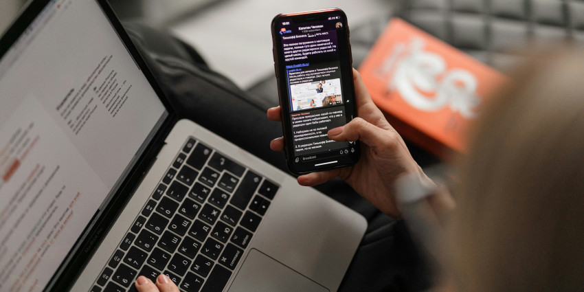 Person reading news on their phone and laptop