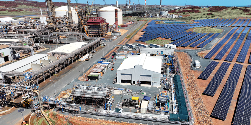 Aerial view of an industrial site with storage tanks, processing structures, and nearby solar panels. 