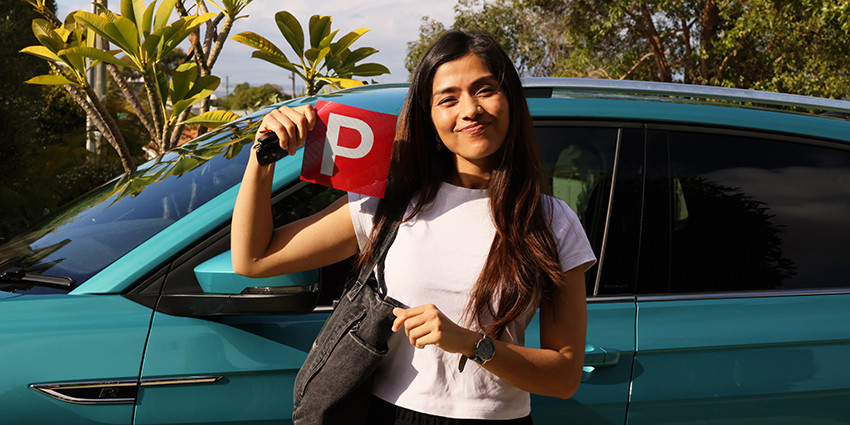 A young driver poses with P plates in front of a vehicle