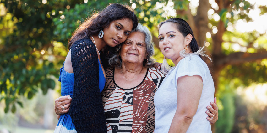 three women, one old and two young, hugging, in an outdoor setting