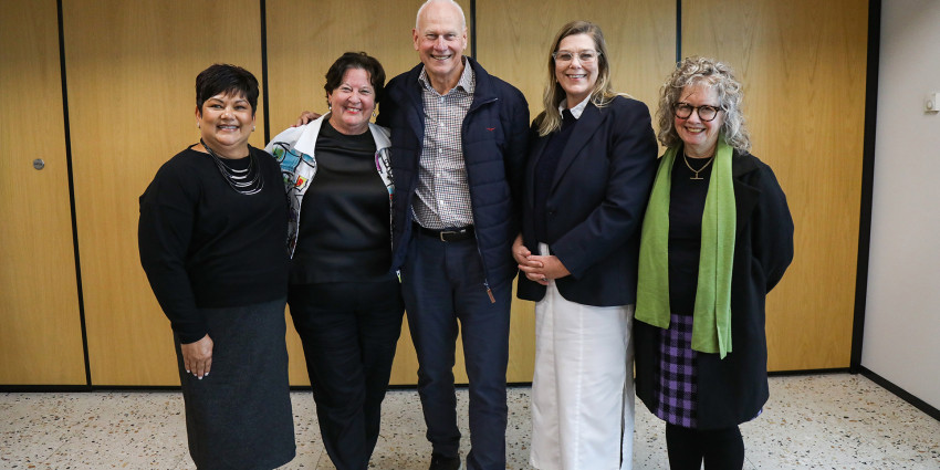 five adult people in an indoor setting smiling