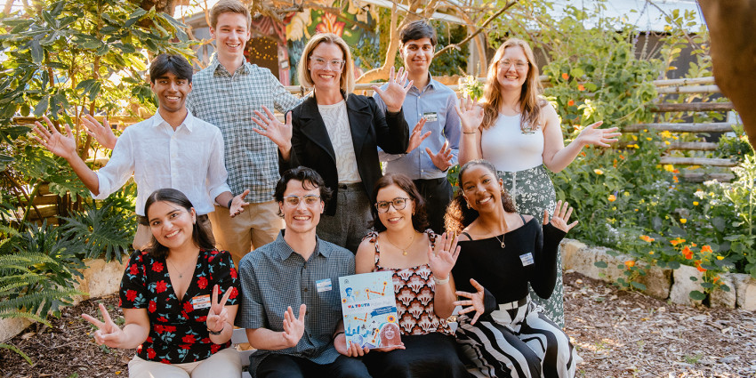 A greoup of young Western Austrlian people and Minister Hannah Beazley in an outdoor garden setting, smiling and holding up a copy of the WA Youth Action Plan