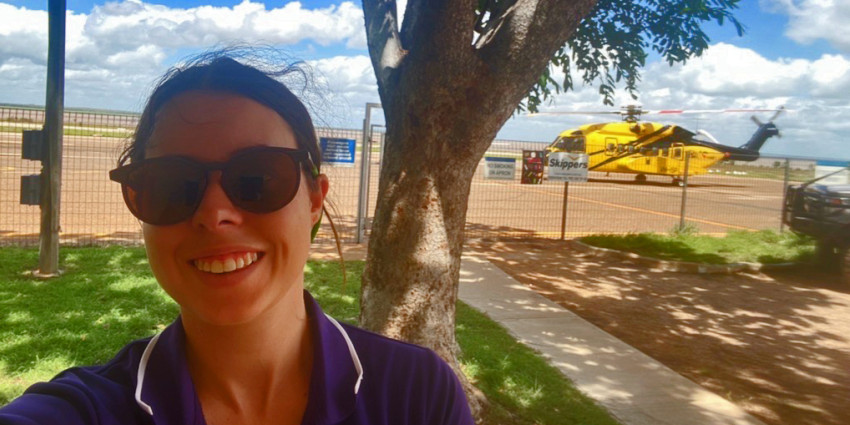 A young woman wearing glasses with a helicopter in the background that she's about to board