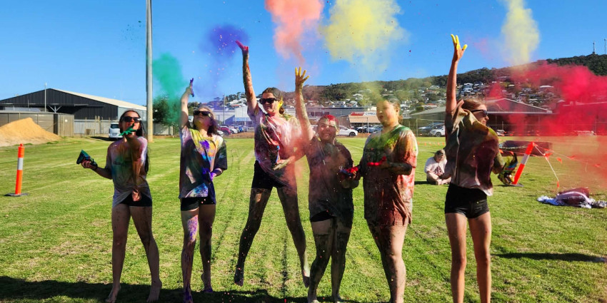 six young adults on a grass oval having fun at the colour run event